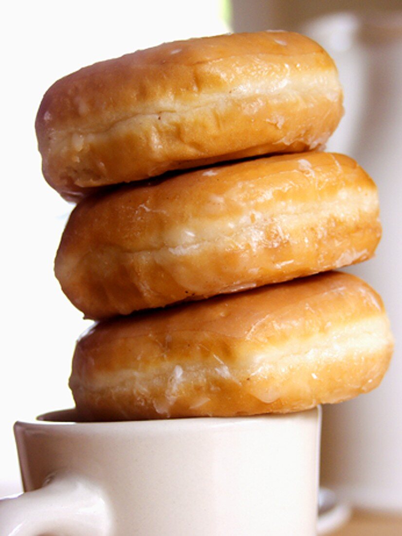 Drei Doughnuts mit Zuckerglasur auf Kaffeetasse