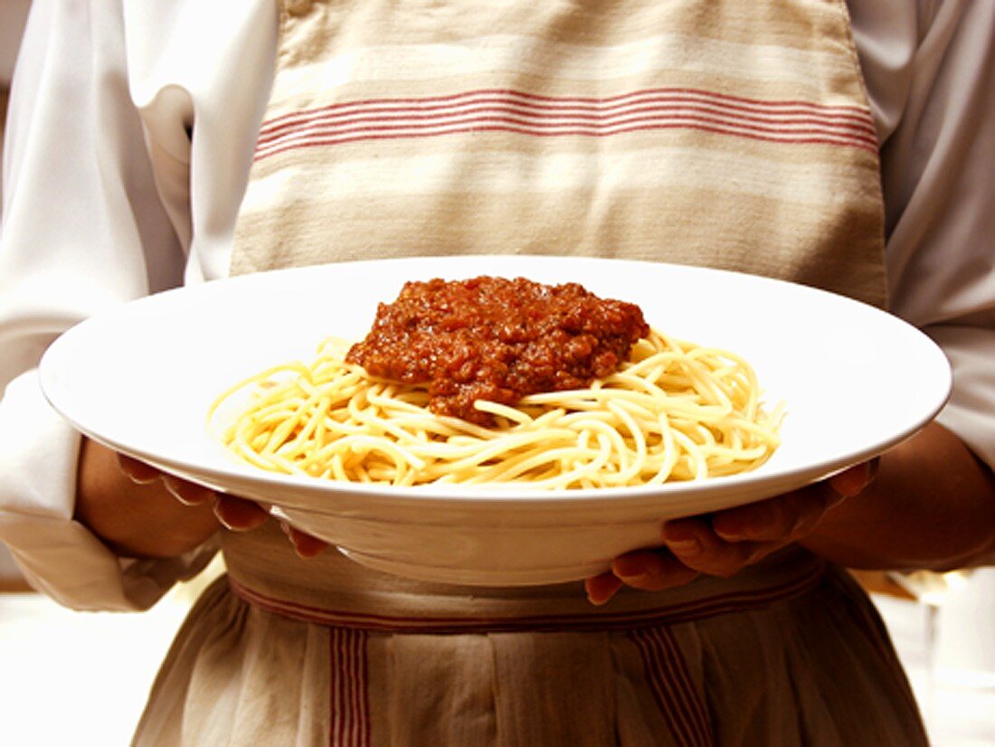 Frau hält grossen Teller mit Spaghetti Bolognese
