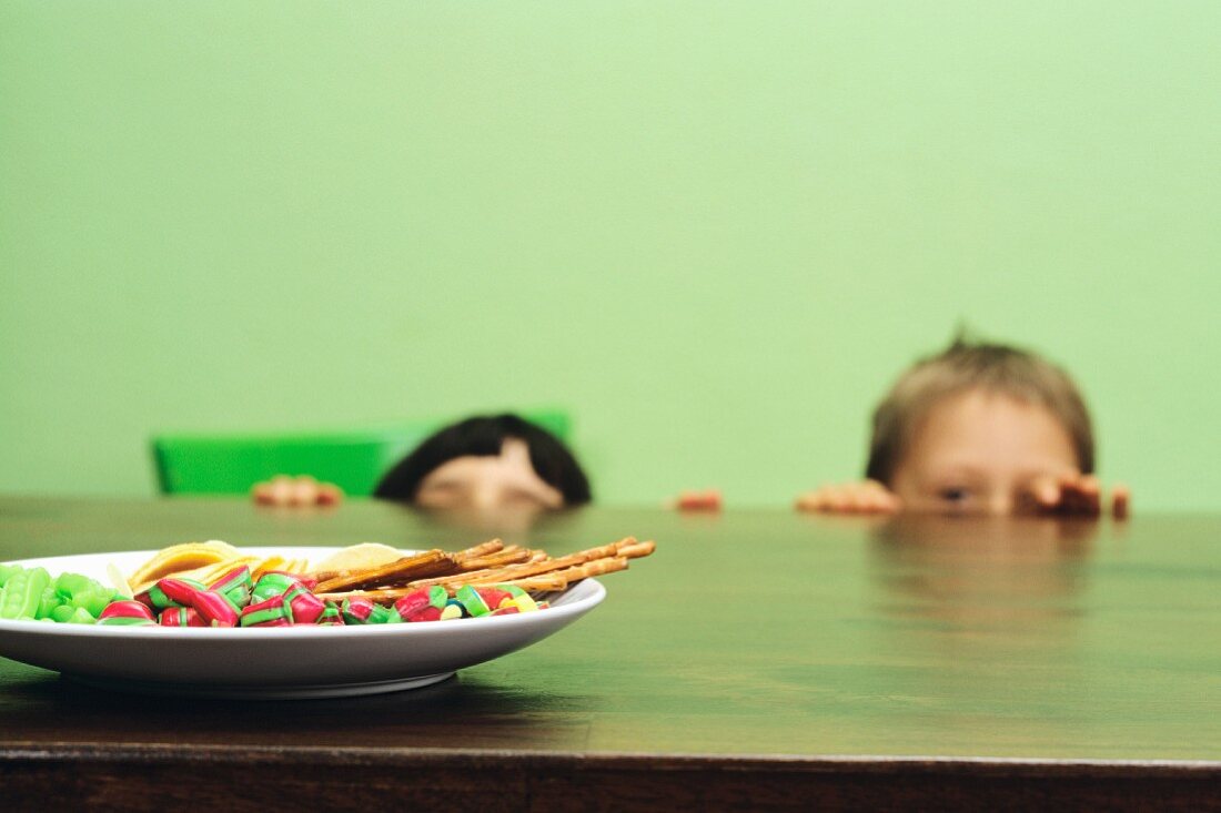 Two boys peeping at sweets over the edge of a table
