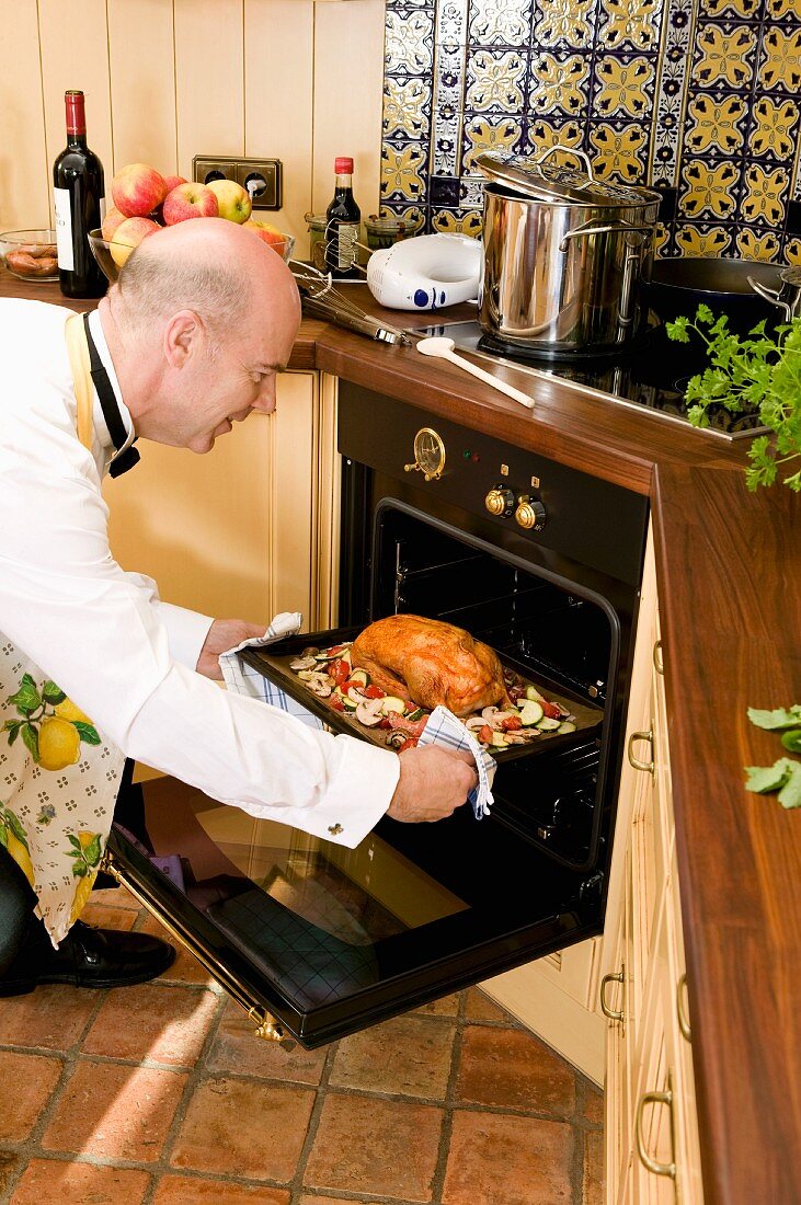 Man dressed for dinner party putting a duck into the oven