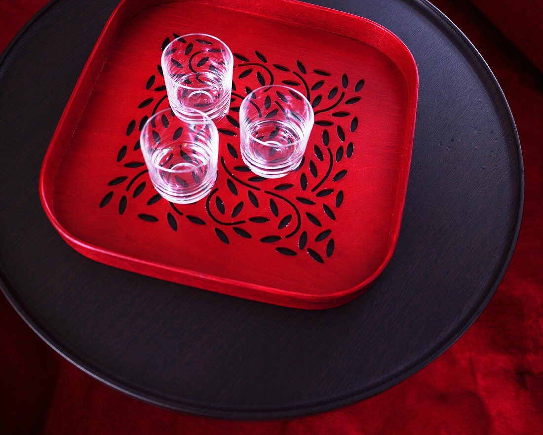 Rotes Tablett mit drei Gläsern auf schwarzem Tisch