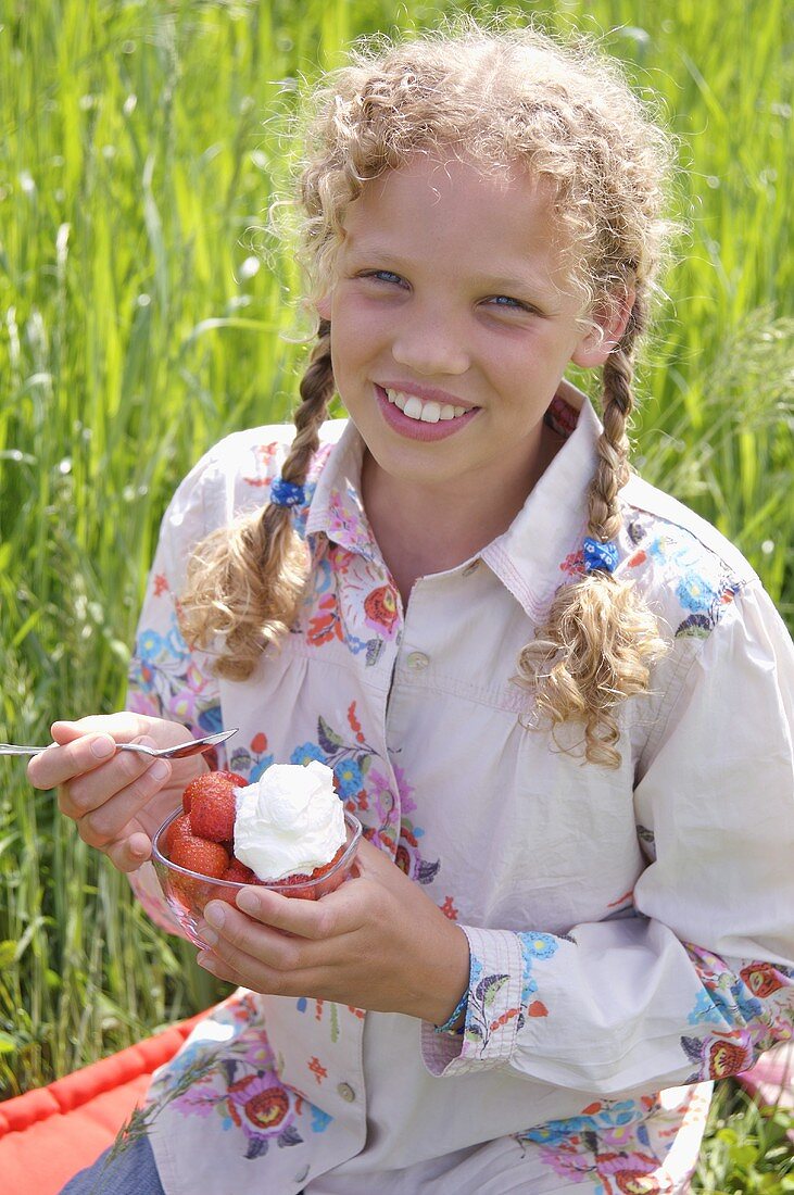 Mädchen isst Erdbeeren mit Sahne im Freien