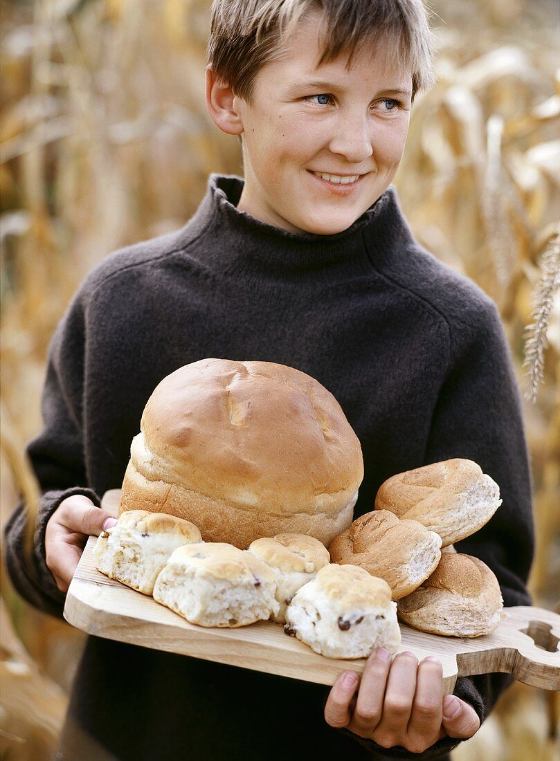 Junge hält Holzbrett mit Brot und Brötchen