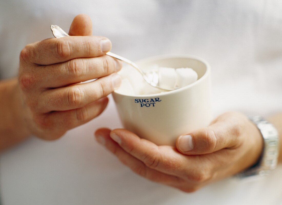 Hands holding a sugar bowl containing sugar cubes