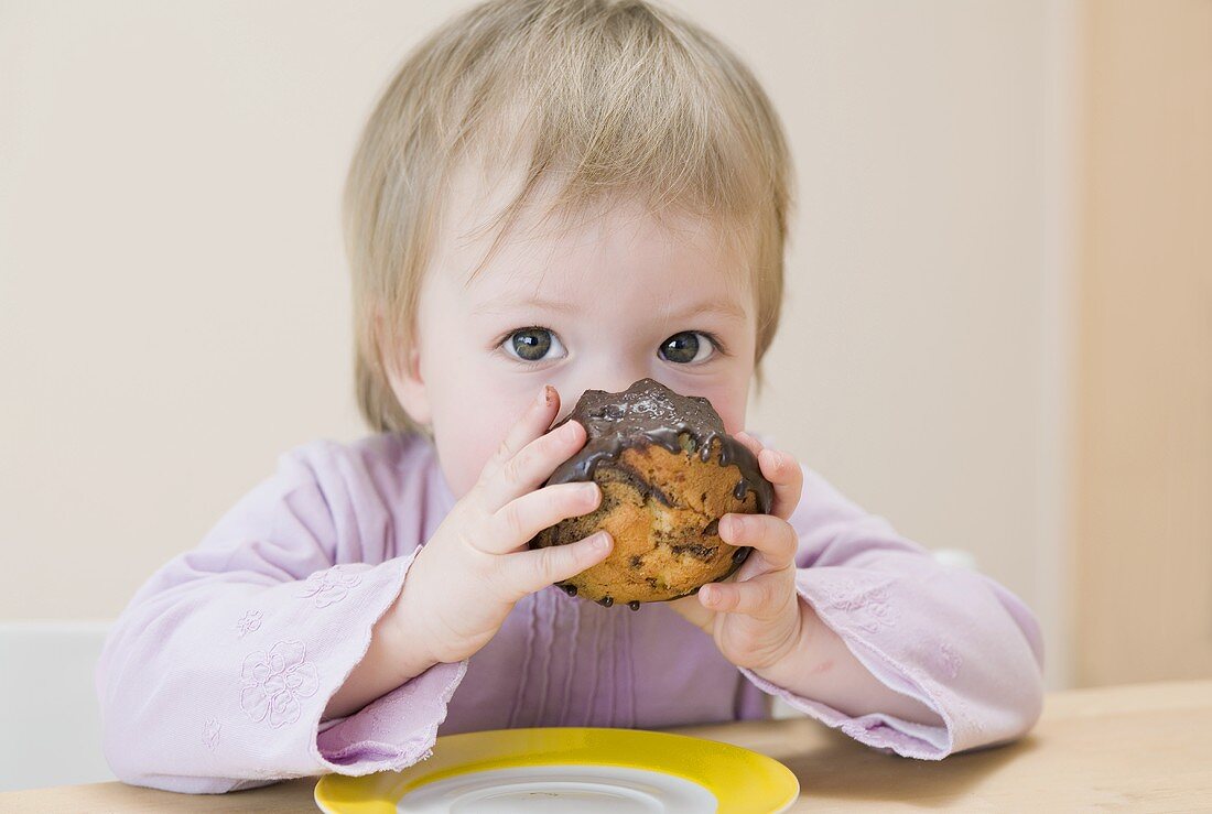 Kleines Mädchen beisst in Mini-Schokoguglhupf