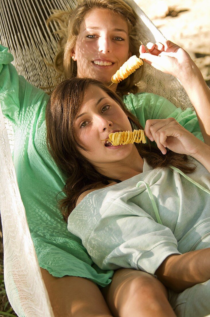 Zwei Freundinnen essen Kartoffelchips in der Hängematte