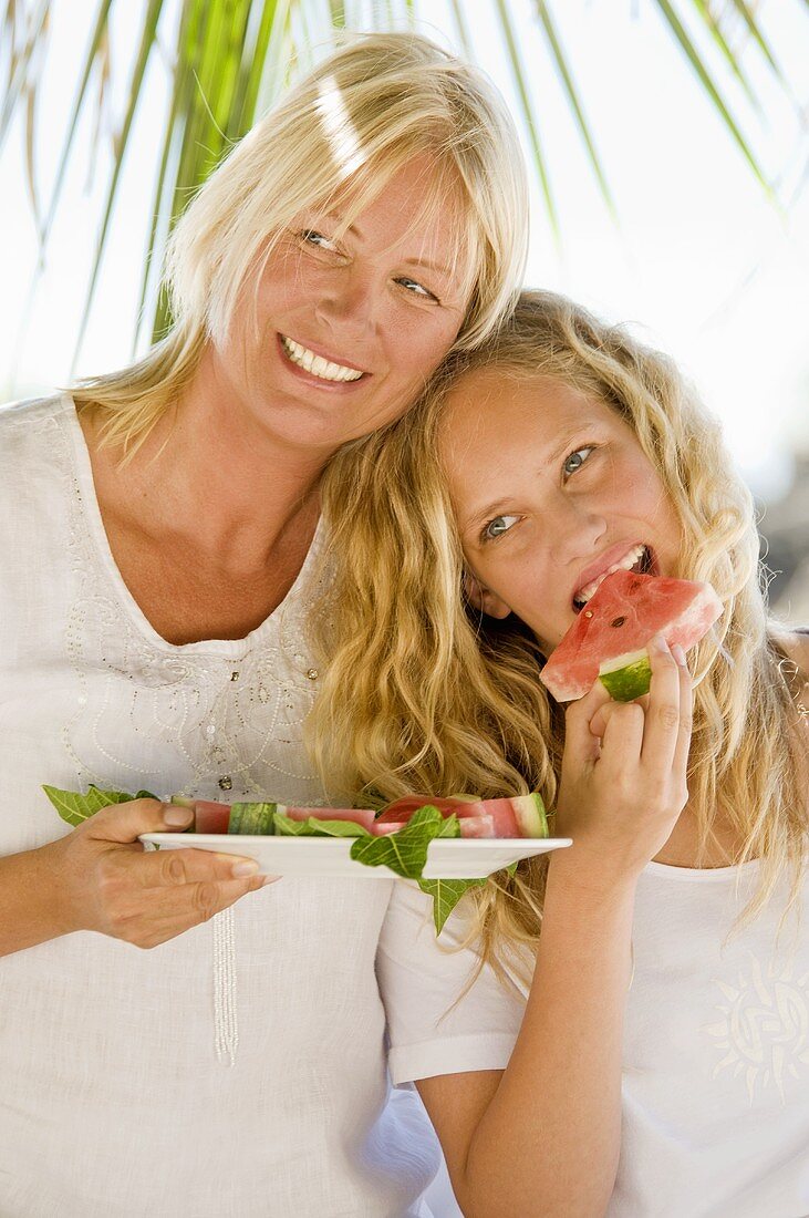 Mother and daughter eating watermelon out of doors