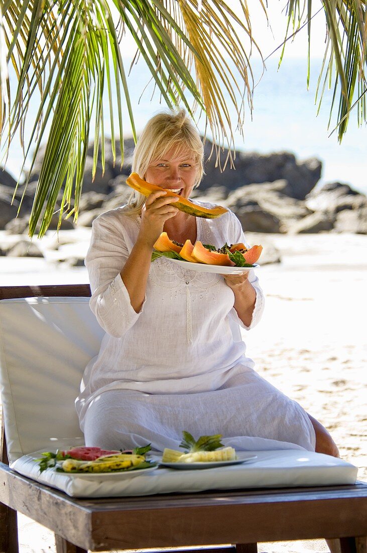 Blonde Frau isst Papaya am Strand