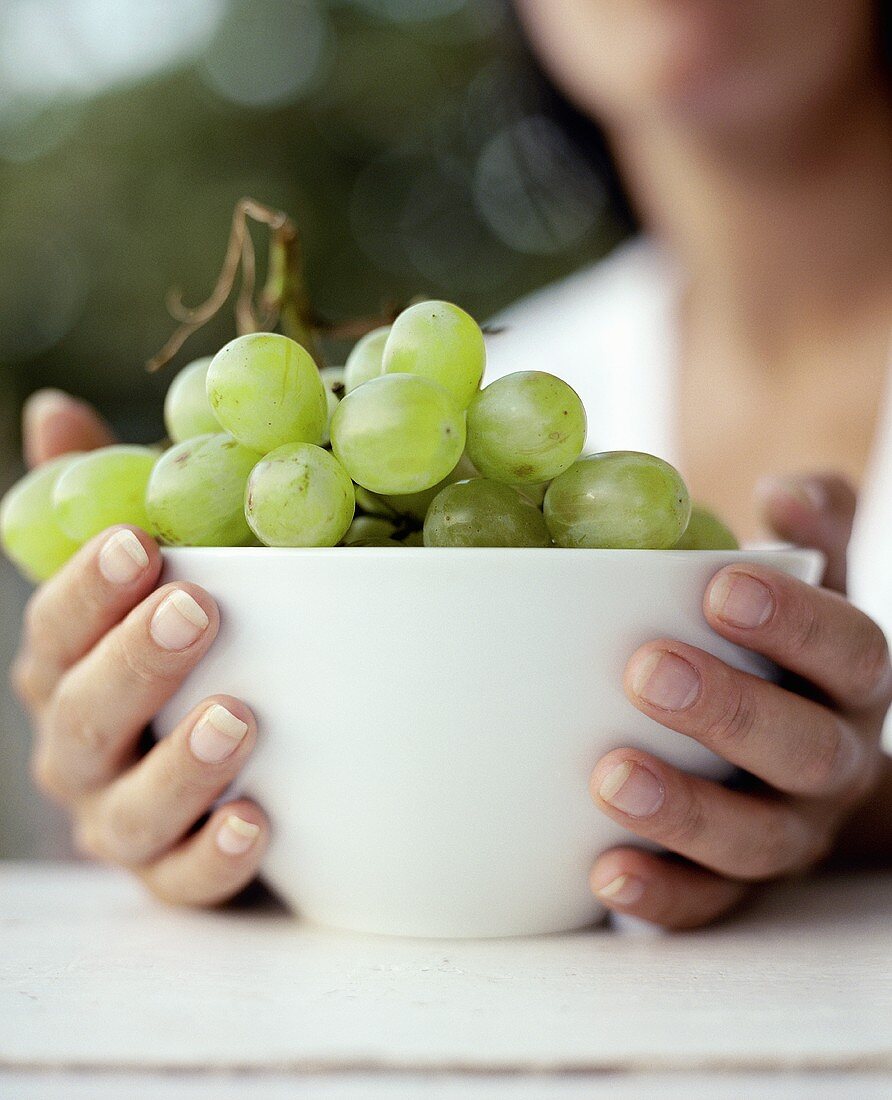 Hands holding a white bowl of grapes