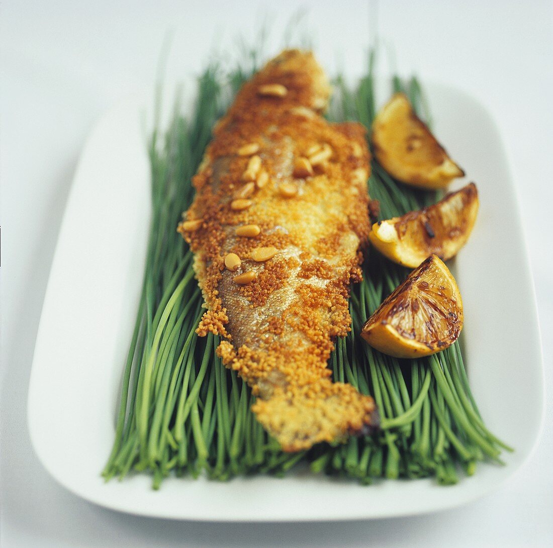 Trout with pine nuts and lemon wedges on chives