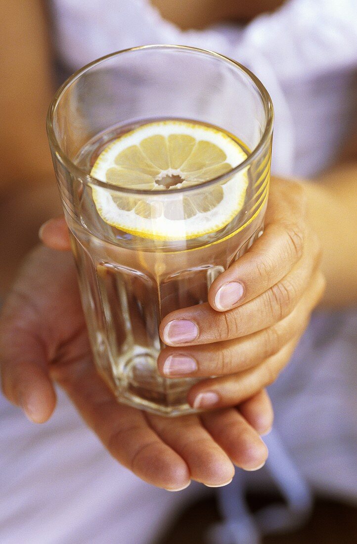 Hands holding a glass of water with a slice of lemon