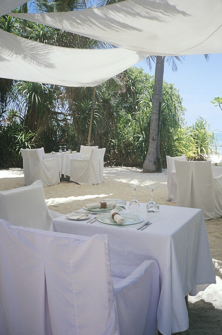 Weiß gedeckte Restauranttische mit Sonnensegeln am Sandstrand