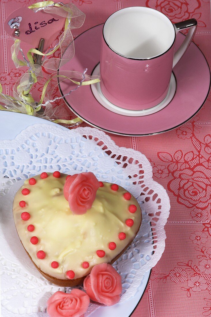 Kleiner herzförmiger Kuchen, Marzipanrosen, rosa Kaffeetasse