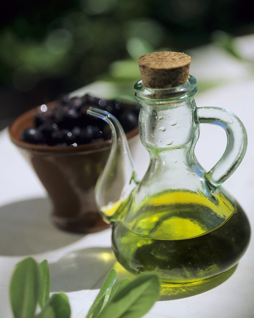 Olivenöl in einer Glaskanne und ein Schälchen Oliven