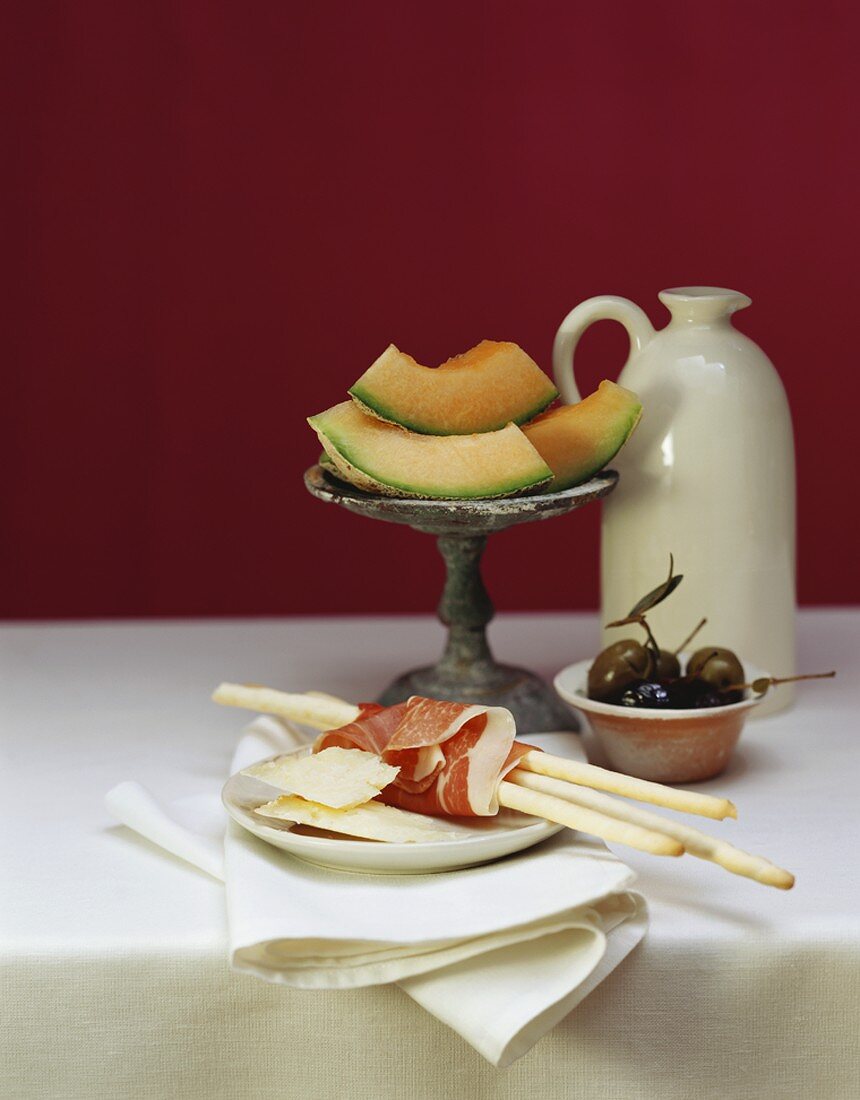 Grissini, ham, cheese, melon, olives on a table