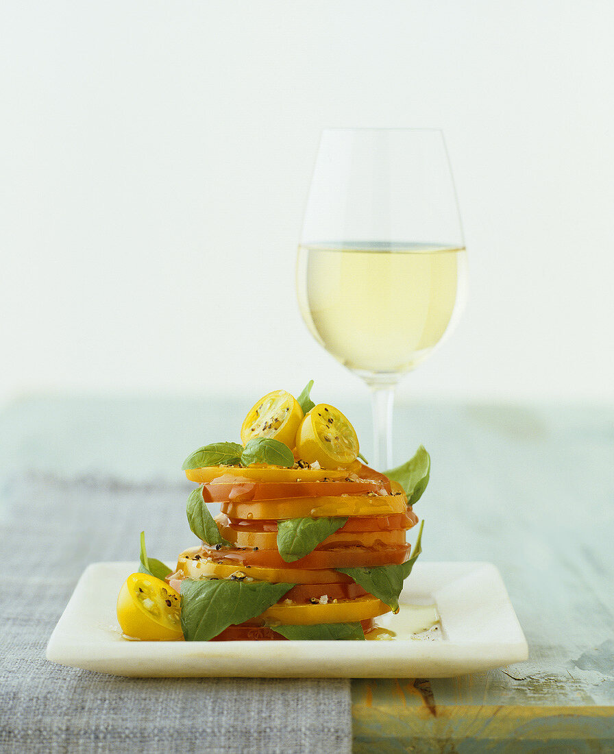 Tomatenscheiben mit Basilikum und ein Glas Weißwein