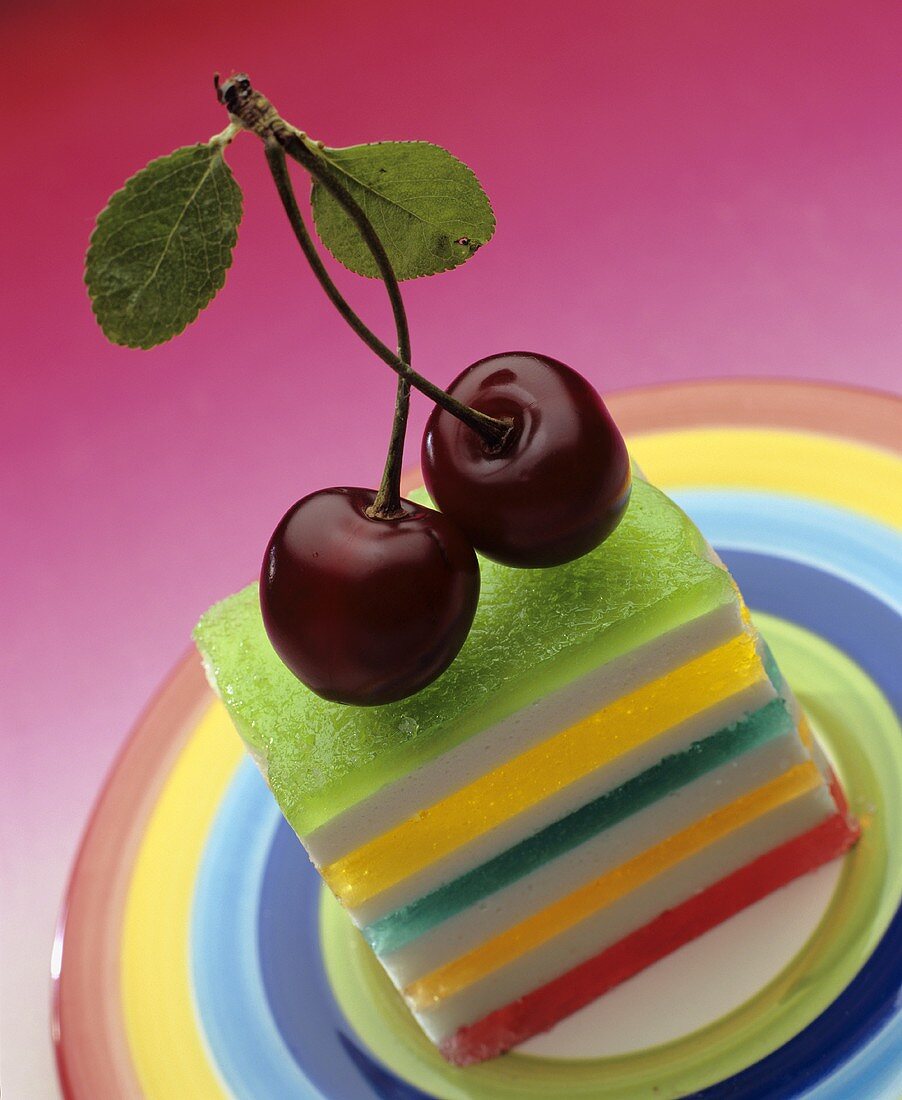 A colourful layer cake topped with two cherries