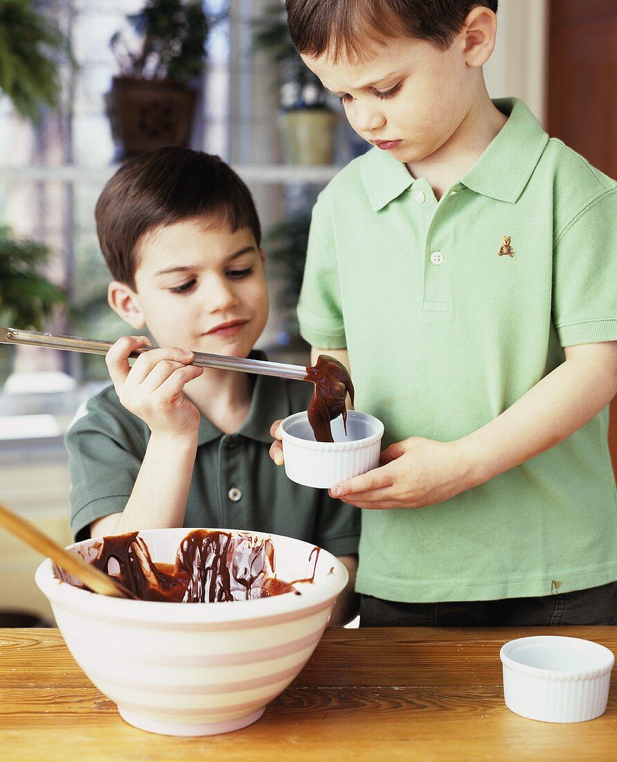 Two boys putting chocolate cake mixture into ramekins