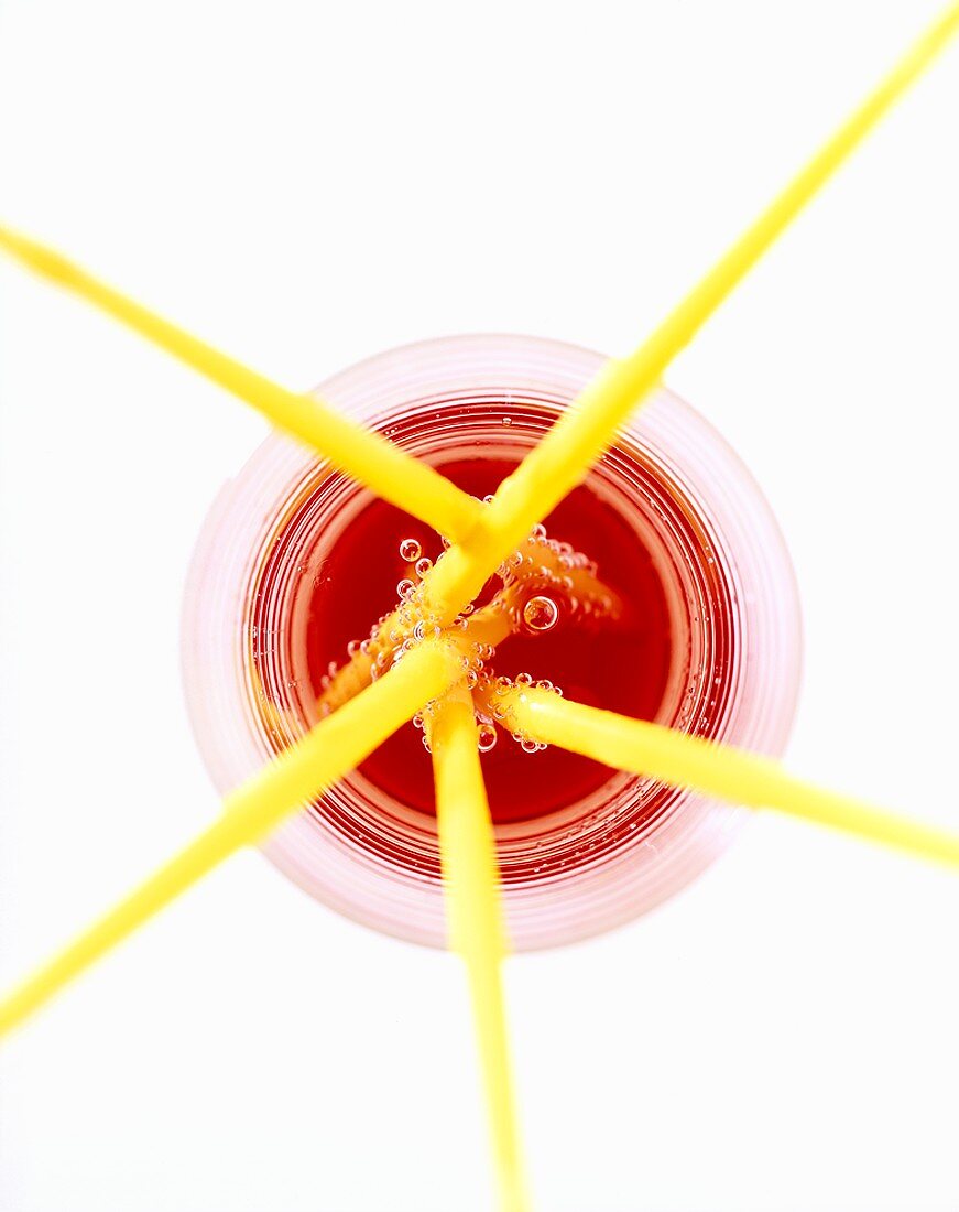 Yellow straws in glass of red drink (from above)