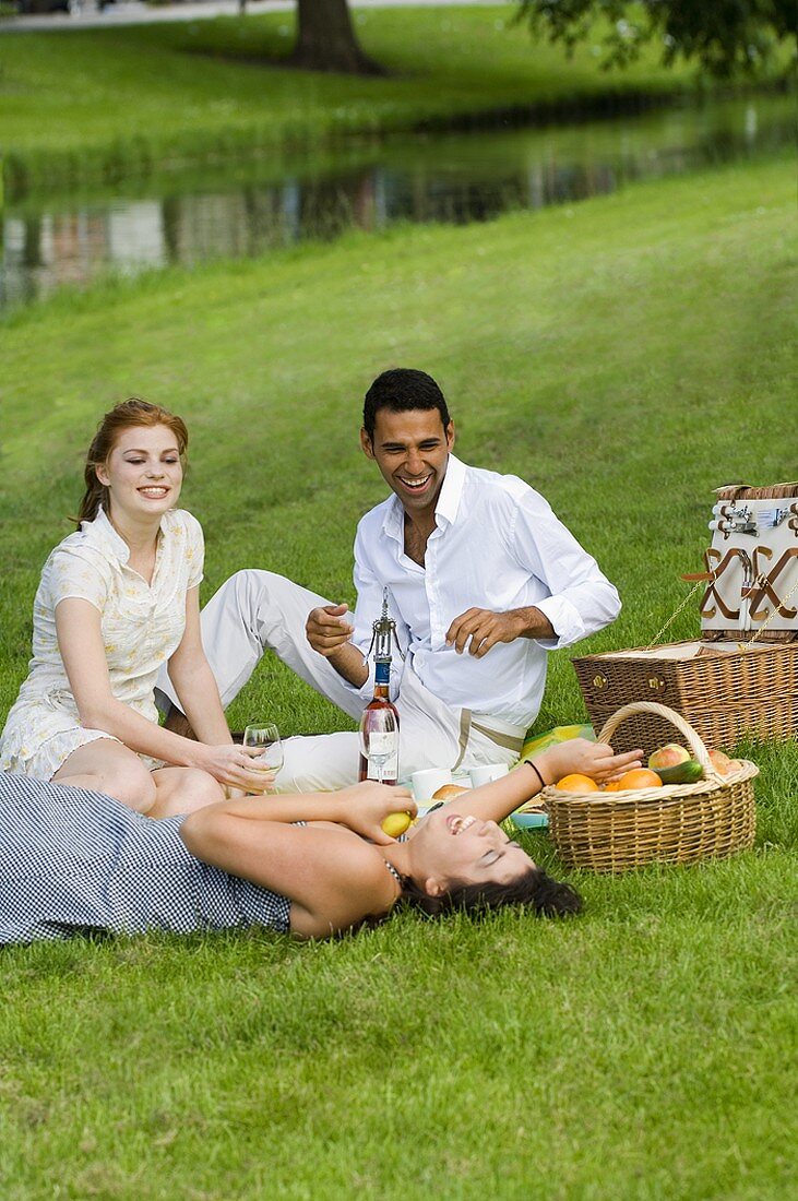 Mann mit zwei Frauen beim Picknick am Bach