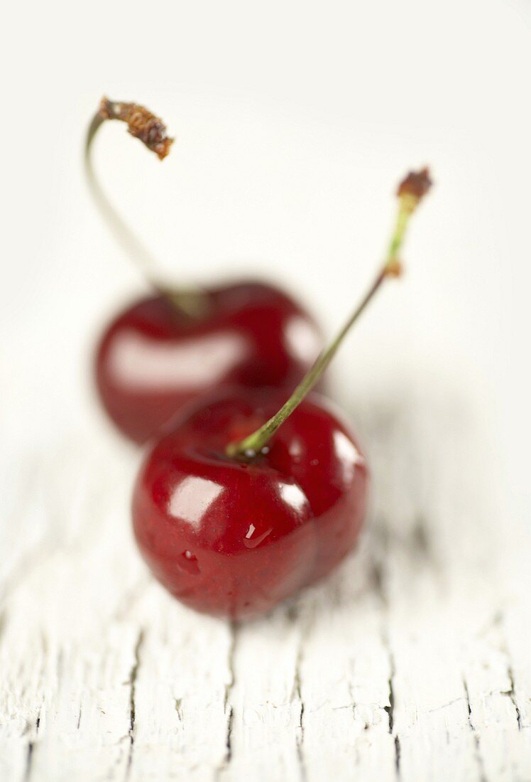 Two cherries on white wooden background
