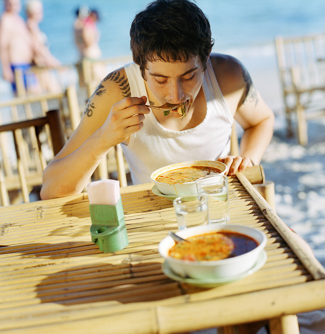 Junger Mann isst Meeresfrüchtesuppe am Strandlokal