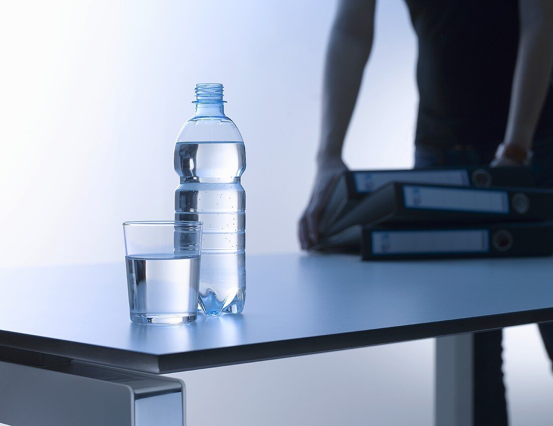 Ein Glas Wasser und eine Flasche Wasser auf Schreibtisch