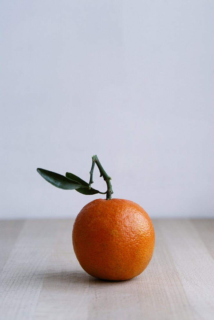 A clementine with leaves on a wooden surface