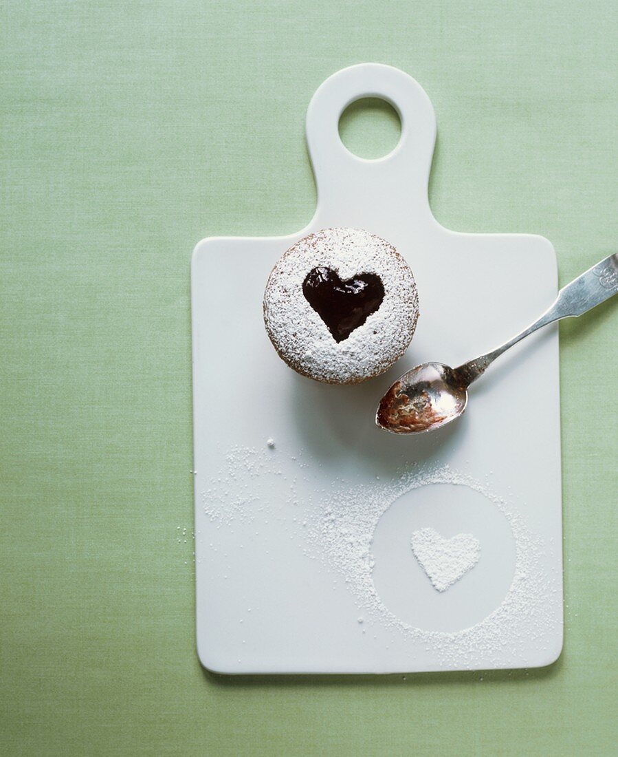 A cupcake with a jam heart on a chopping board