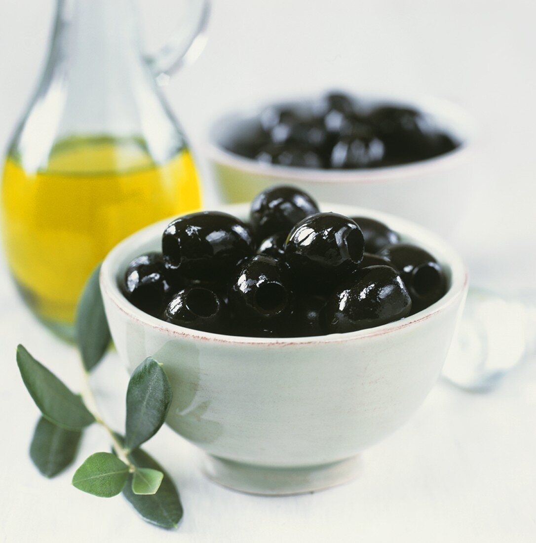 Schwarze, eingelegte Oliven mit Oilvenzweig und Olivenöl