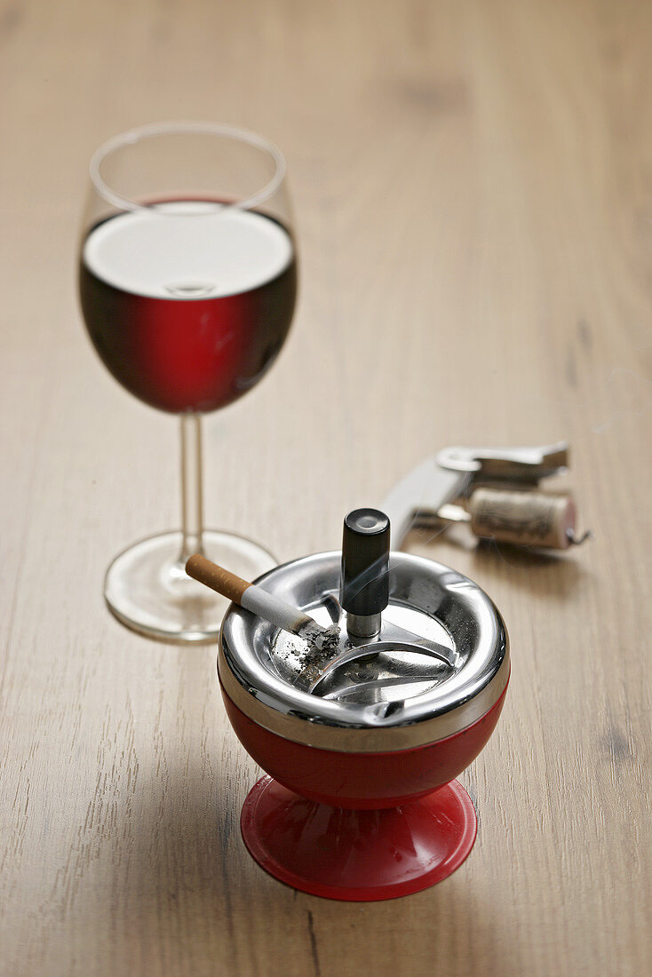 A glass of red wine with a cigarette in an ashtray