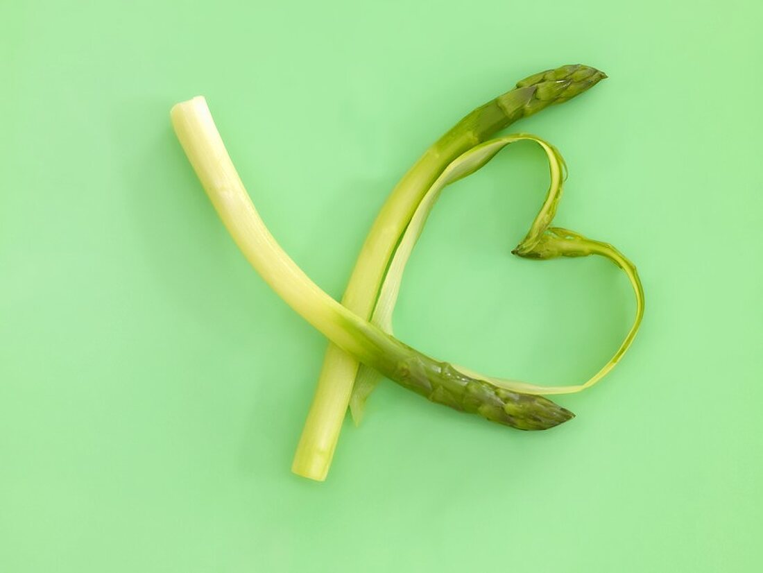 Two peeled spears of green asparagus, peelings forming a heart