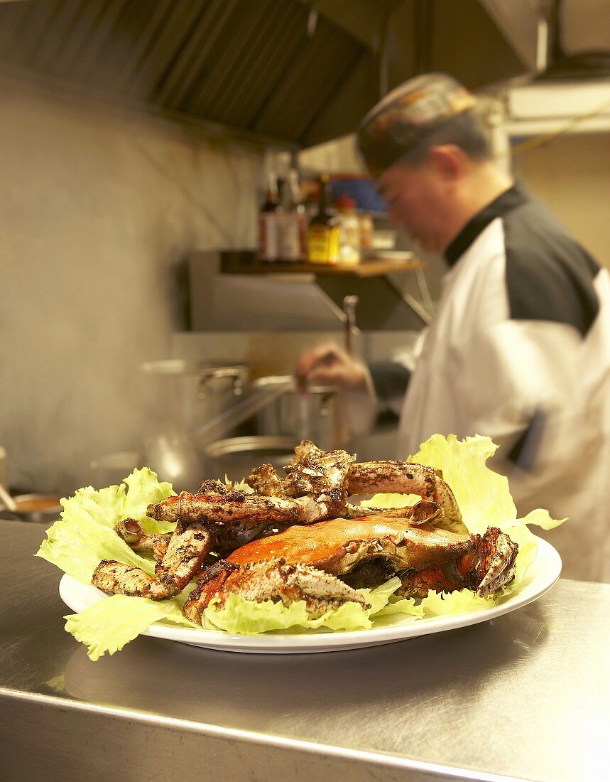 Whole crab on lettuce leaves, chef in background (Asia)