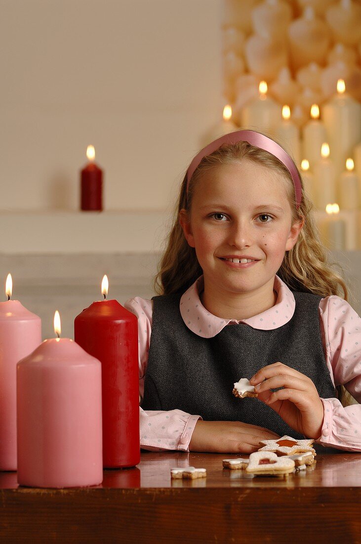 Mädchen sitzt am Tisch mit Kerzen und Weihnachtsplätzchen