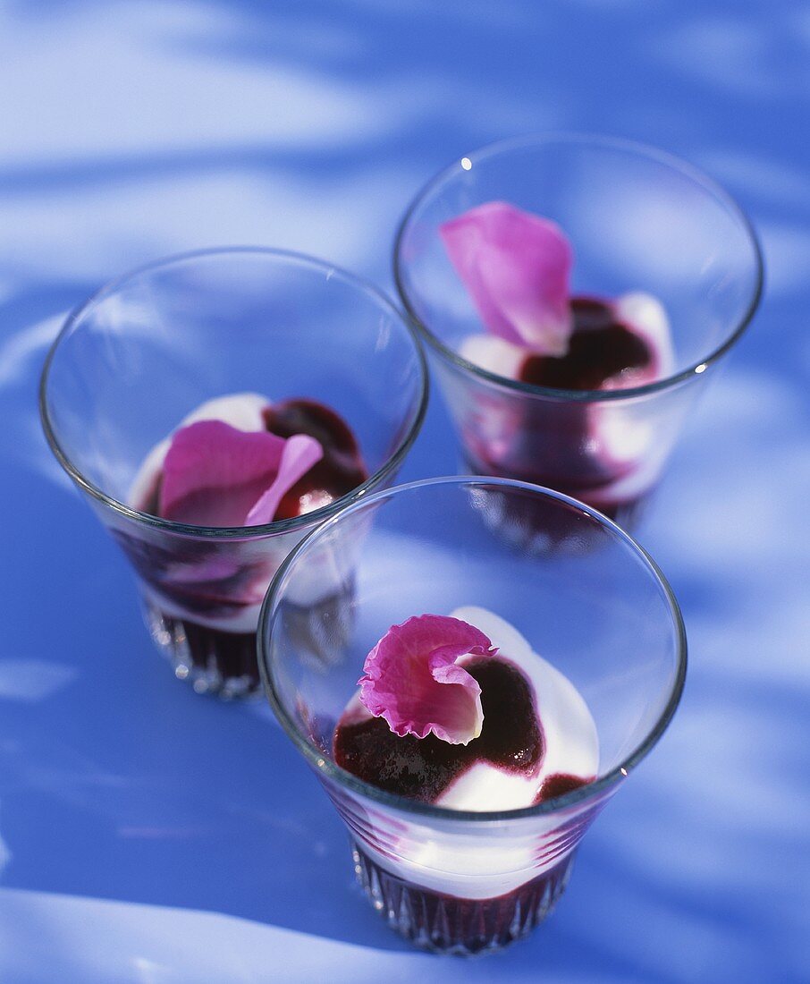 Three glasses of yoghurt with berry sauce and rose petals