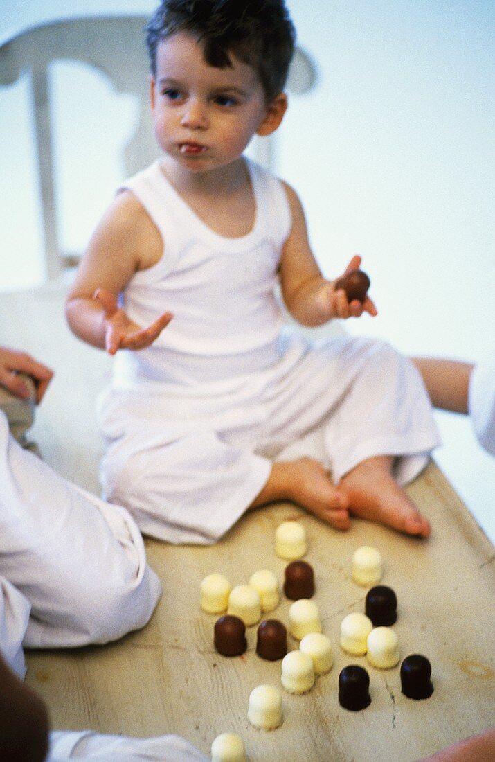 Little boy sitting on table, eating chocolate-coated marshmallows