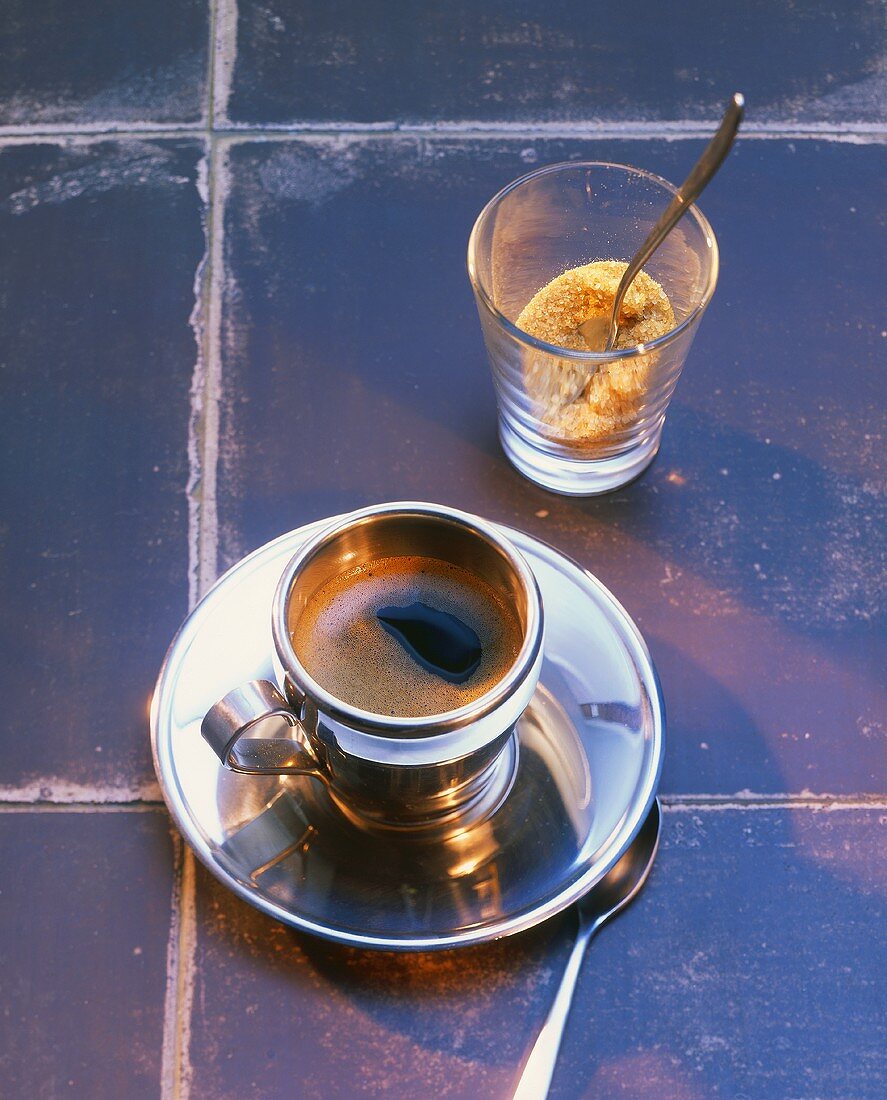 Espresso in Silbertasse mit braunem Zucker auf Kacheln