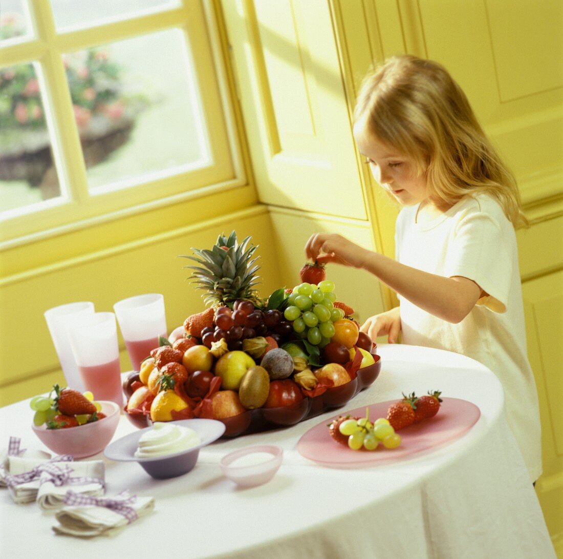 Blondes Mädchen nimmt Erdbeere aus Obstschale vom Tisch