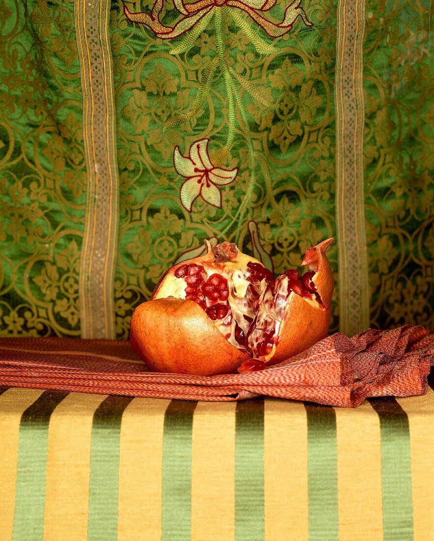 Ein aufgebrochener Granatapfel vor orientalischem Stoff