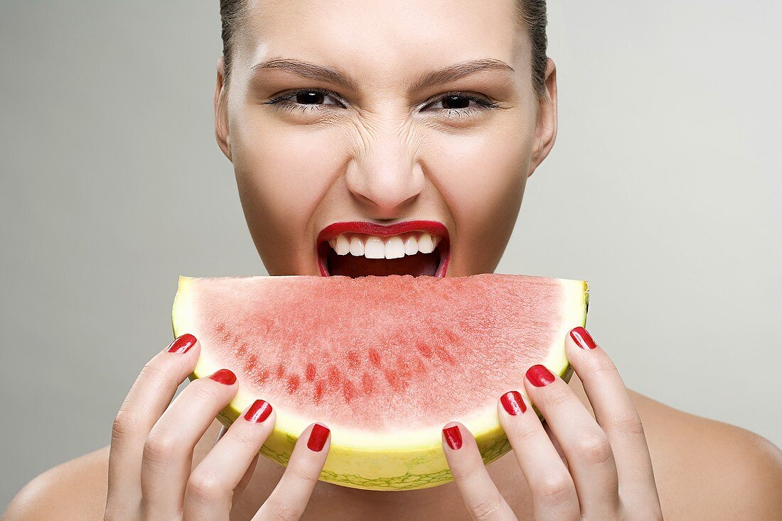 A young woman biting a watermelon