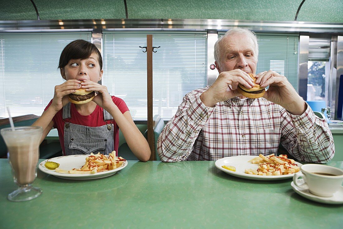 Mädchen und älterer Herr essen Burger in einem Diner