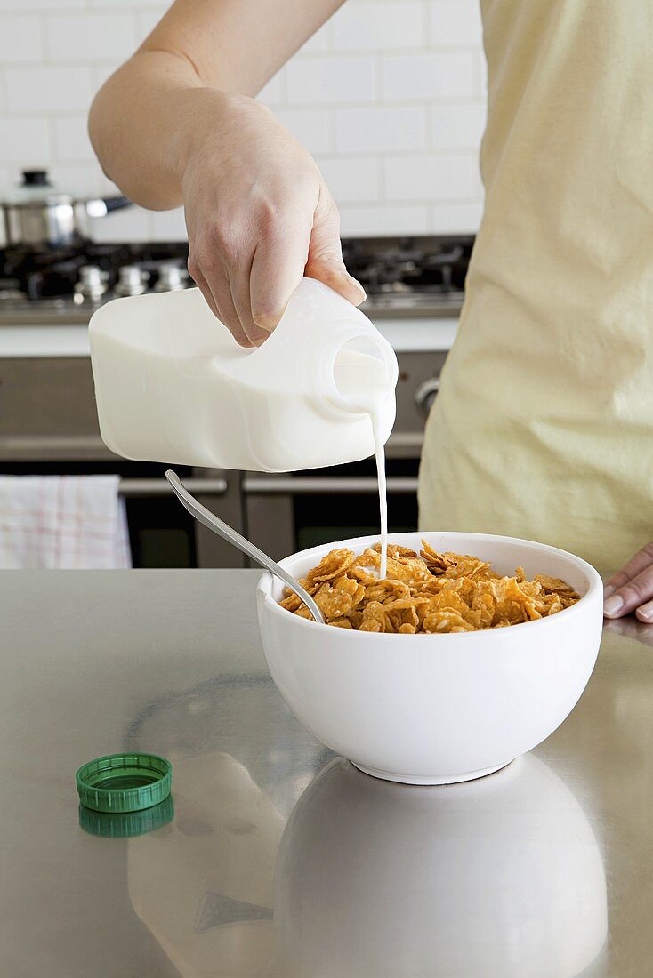 Frau gießt Milch auf Cornflakes