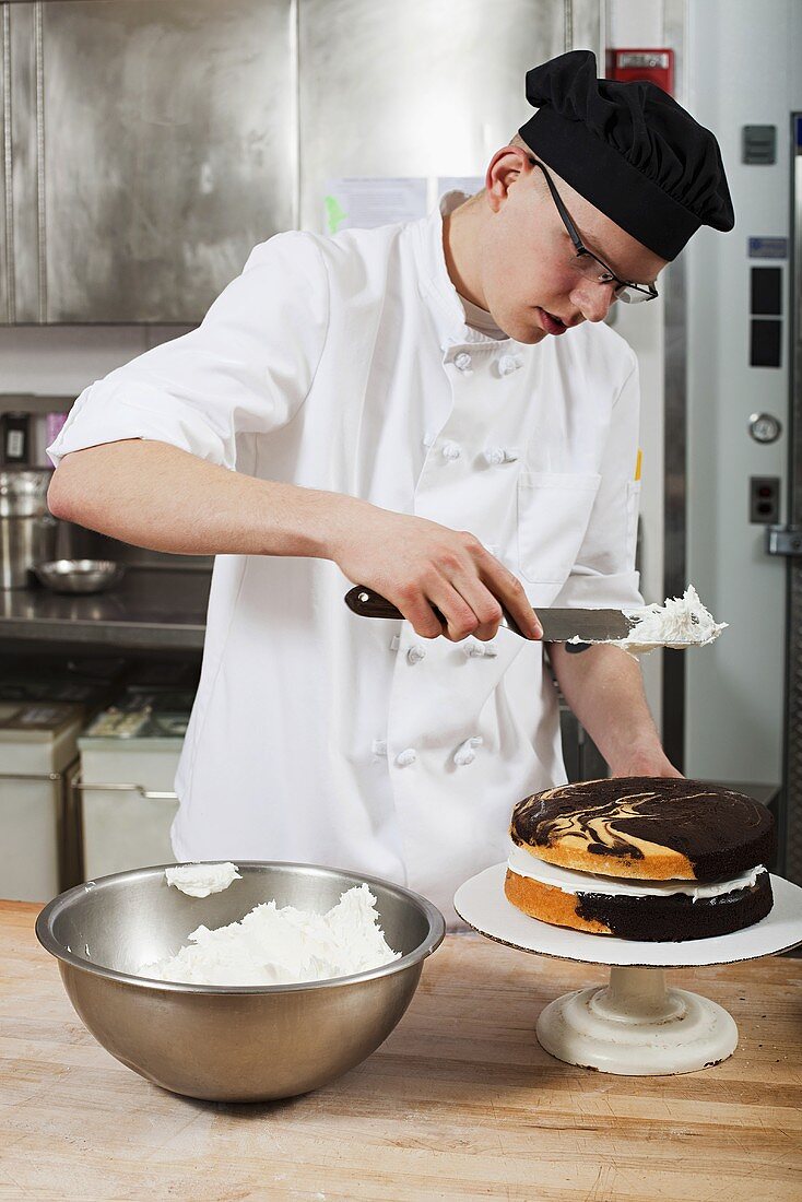 A confectioner icing a cake in a commercial kitchen