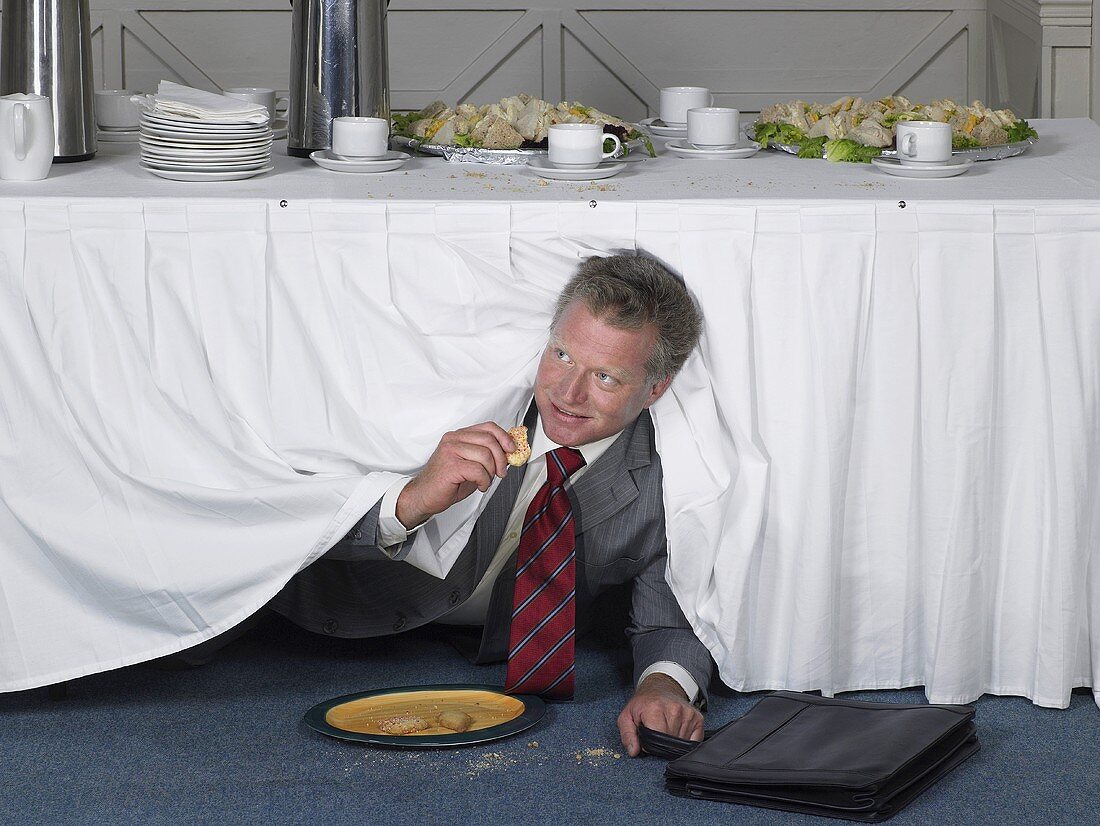 A businessman in a suit eating under a table