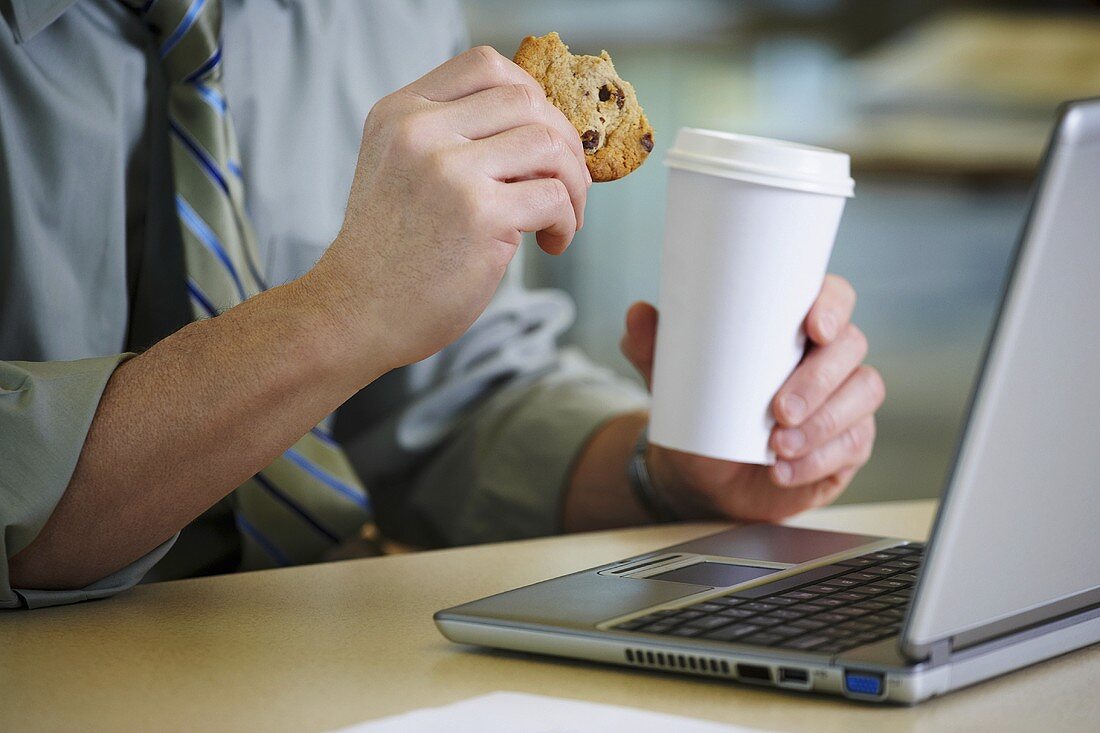 Mann am Schreibtisch mit Kaffee und einem Cookie