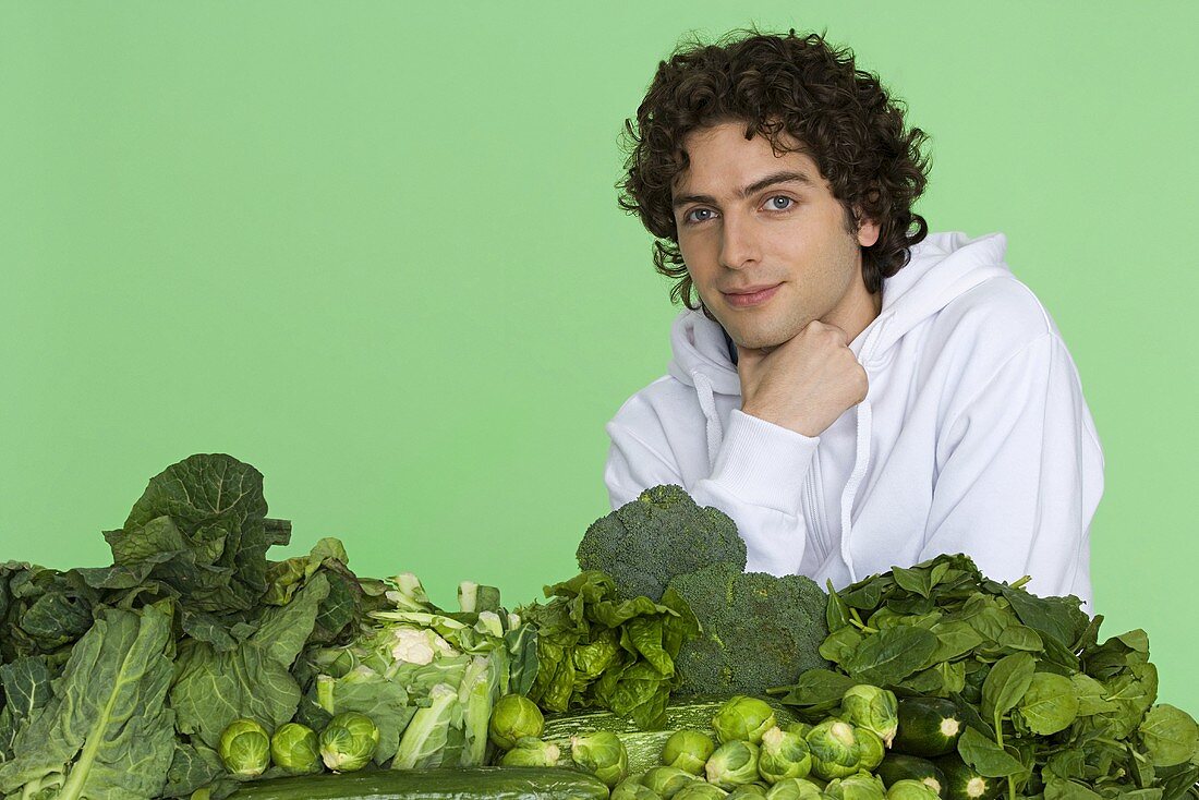 A young man with pile of green vegetables