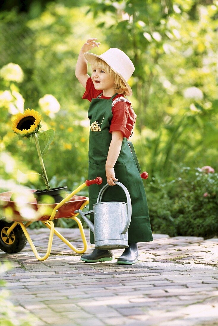 A little girl dressed as a gardener holding a watering can and a sunflower