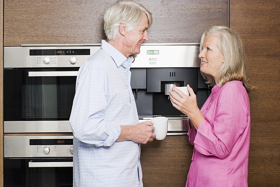 A middle aged couple standing in a kitchen with cups of coffee