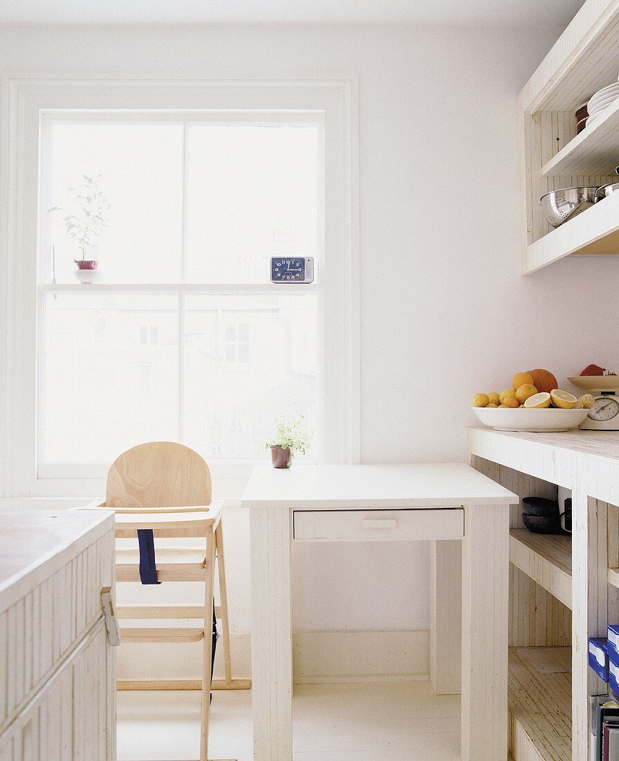 A kitchen with a high chair and a dining table under the window