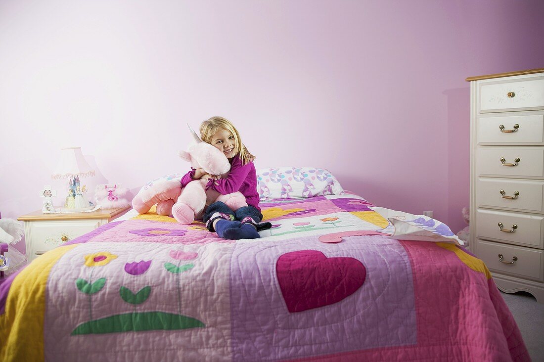Mädchen auf Bett mit fröhlicher Steppdecke beim Herzen eines Kuscheltiers
